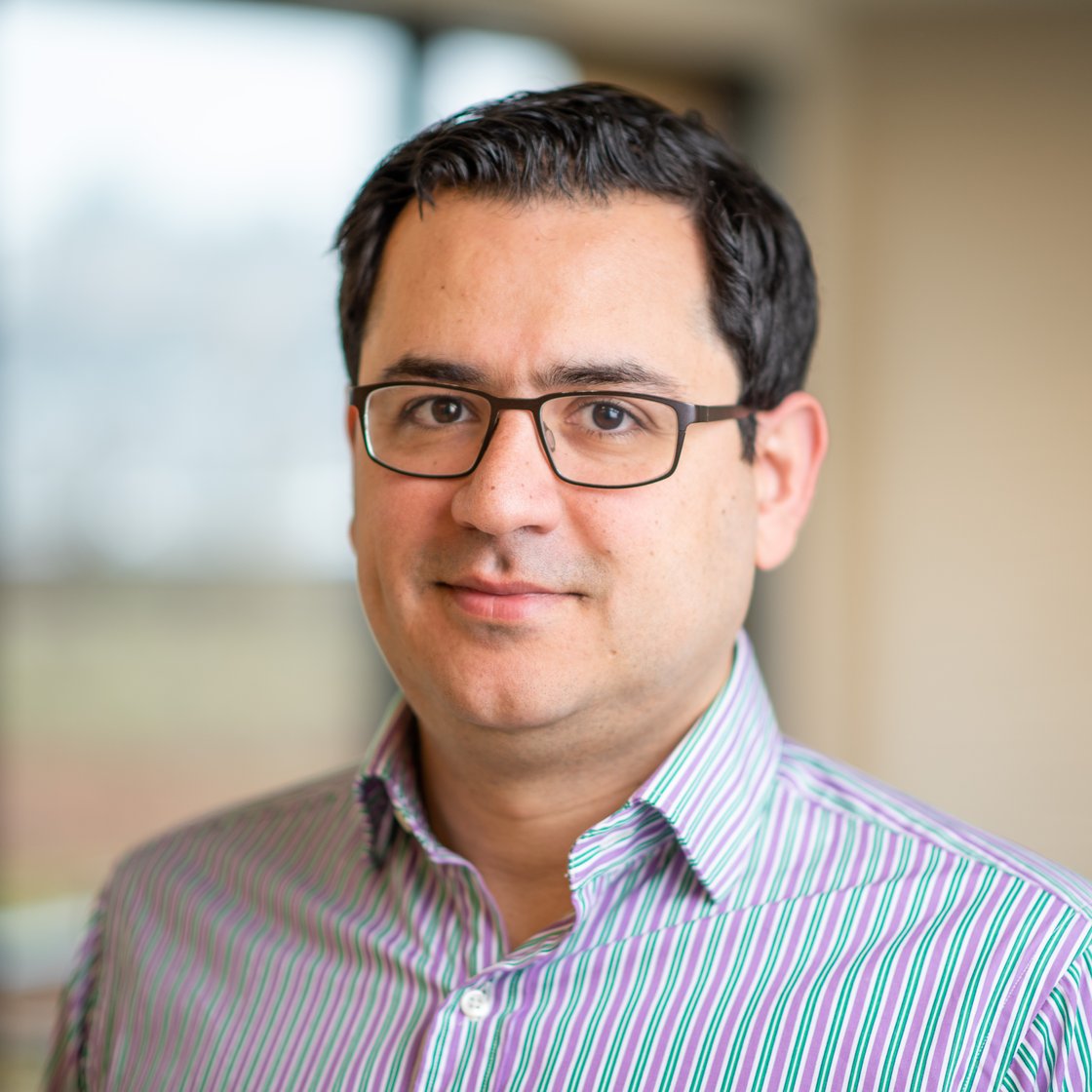 Ali Farhadi is pictured with dark combed-back hair wearing a striped shirt, bronze eyeglasses.